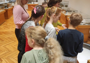Uczestnicy wycieczki słuchają jak pani z muzeum opowiada o eksponatach