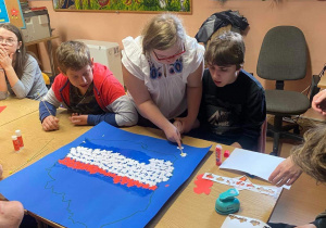 Filip, Joanna i Dominik współpracując wyklejają kontur Polski