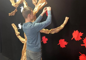 Chłopiec przypina czerwony liść do drzewa